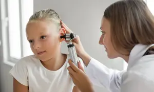 Lekarz od uszu bada ucho dziewczynki otoskopem.