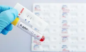 Ręka w rękawiczce trzyma probówkę z oznaczeniem "H. pylori" i zaznaczonym wynikiem dodatnim, obok test kasetkowy z dwoma paskami.