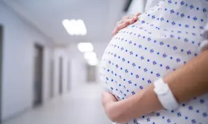 Brzuch kobiety w szpitalnej koszuli w niebieskie wzory, ręka na nim. Stan przedrzucawkowy.