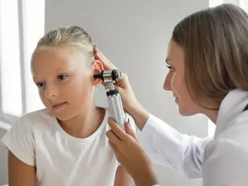 Lekarz od uszu bada ucho dziewczynki otoskopem.