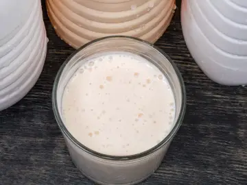 Szklanka z napojem, który przeszedł fermentację mlekową, otoczona pojemnikami.