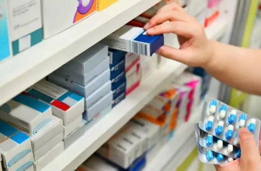 Ręka wybiera lek z aptecznej półki. Zastanawiasz się, po jakim czasie działa antybiotyk? To zależy od wielu czynników.