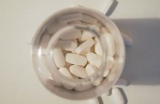 Białe tabletki, jak Tegretol, wypełniają przezroczysty pojemnik. Kilka tabletek leży obok.